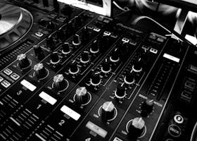 Black and white close-up of a DJ's audio mixing console with knobs and controls.